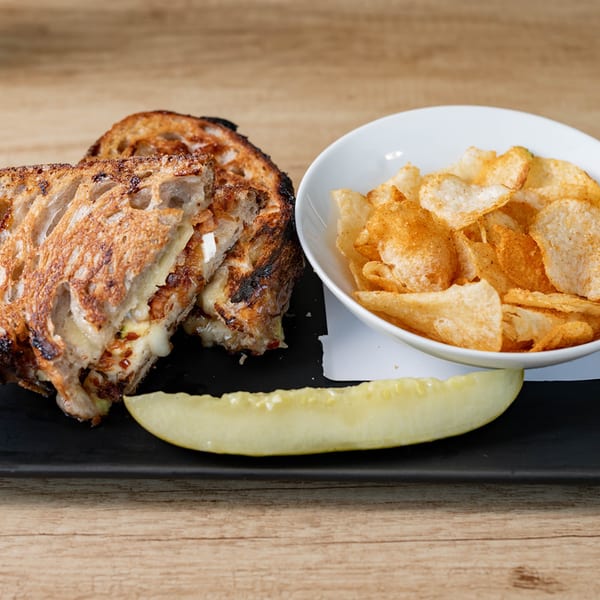 Grilled cheese sandwich, potato chips, and a pickle spear on a black plate.
