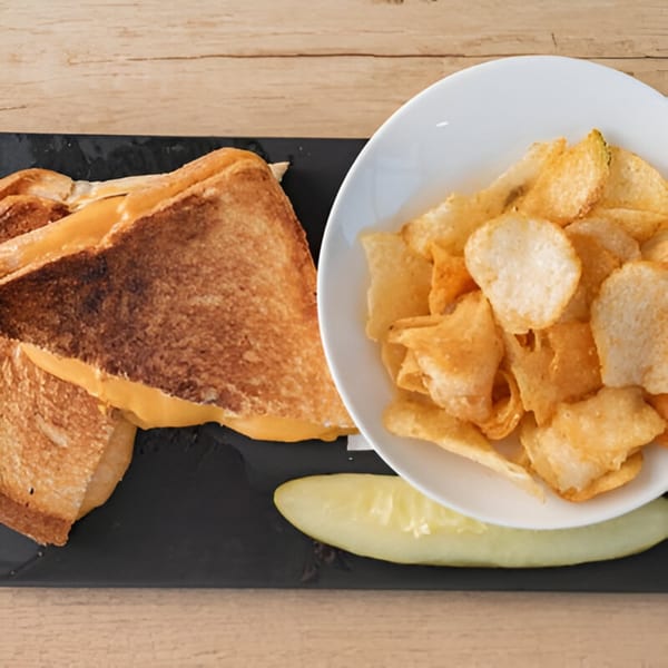 Grilled cheese sandwich with a side of potato chips and a pickle spear on a black plate.