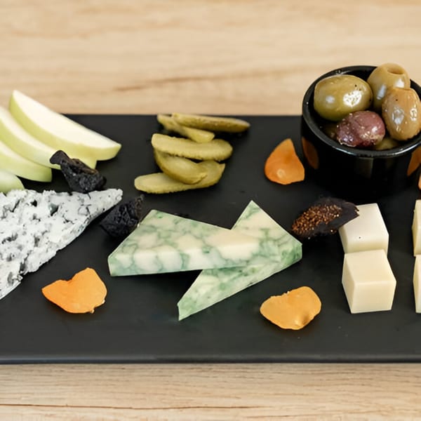 A black platter of Artisan Beer and Cheese's cheese, pickles, olives, dried fruit, and apple slices.