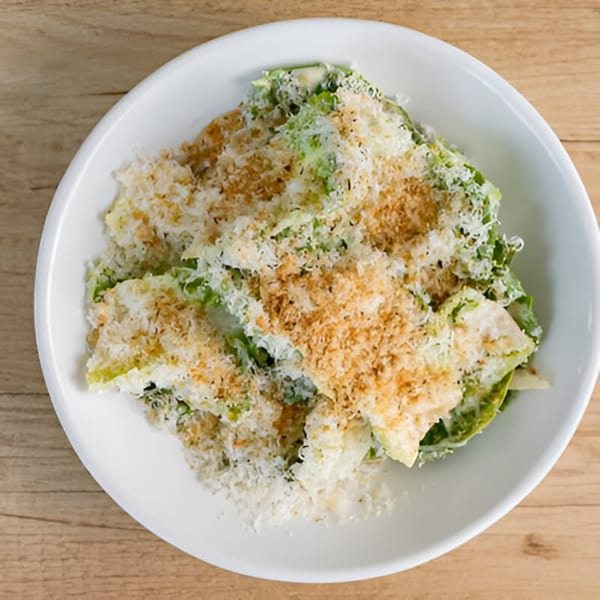 Caesar salad with green lettuce, white cheese, and brown breadcrumbs in a white bowl.