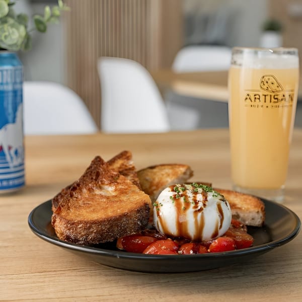 Burrata with tomatoes, toasted bread, and a glass of Artisan Beer on a wooden table.