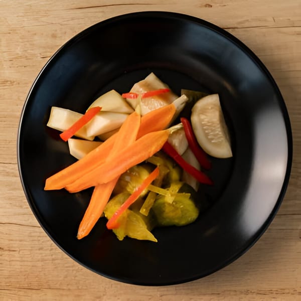 A black plate filled with pickled vegetables including carrots, cucumbers, and peppers.