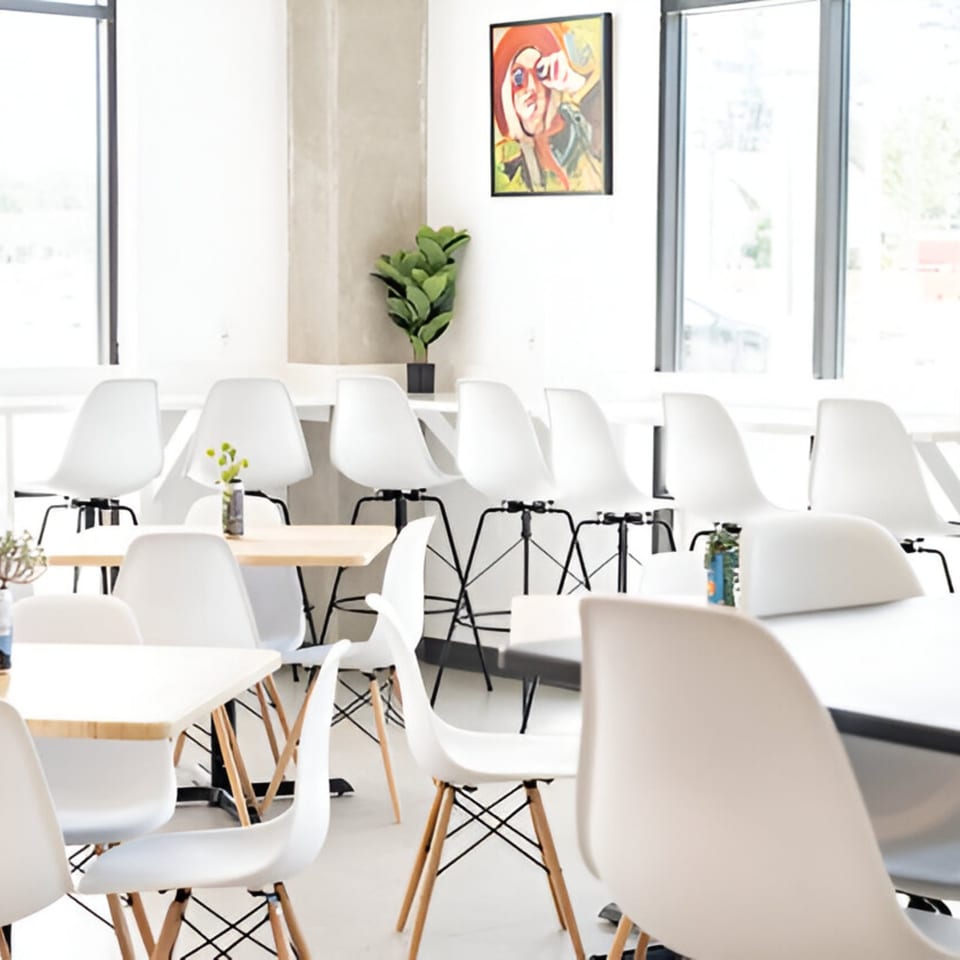 Bright, modern bar interior with white chairs, light wood tables, and large windows.
