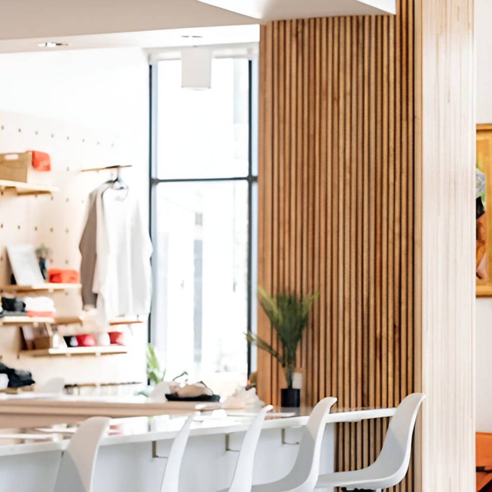 A modern bar interior with white stools, wooden slat walls, and shelves displaying merchandise.
