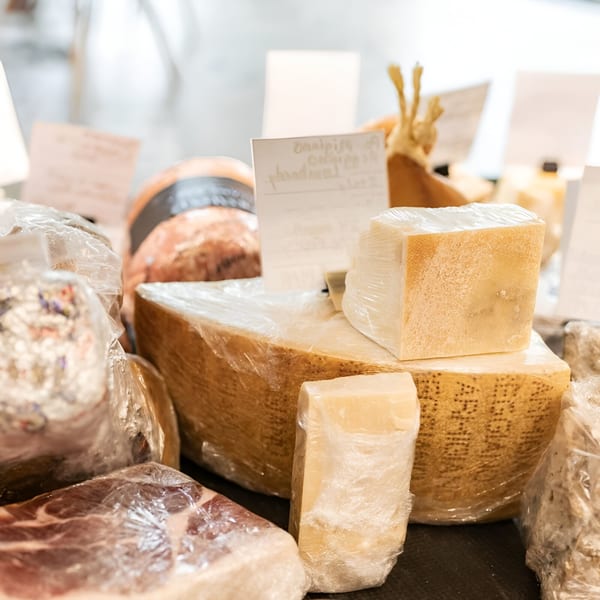 Assortment of artisan cheeses and cured meats, wrapped in plastic, displayed at Artisan Beer and Cheese.